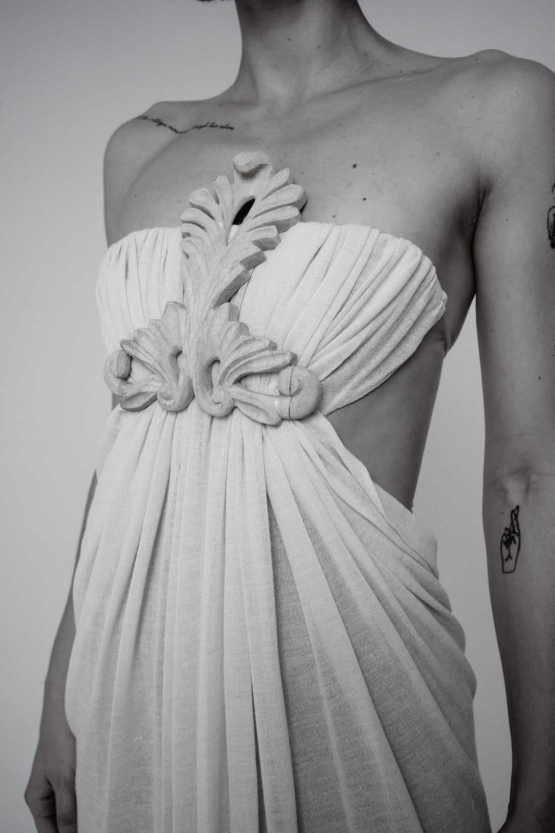 ALISADUDAJ craftsmanship: black and white close-up of a draped one-shoulder bodice with a sculptural hand-worked floral appliqué