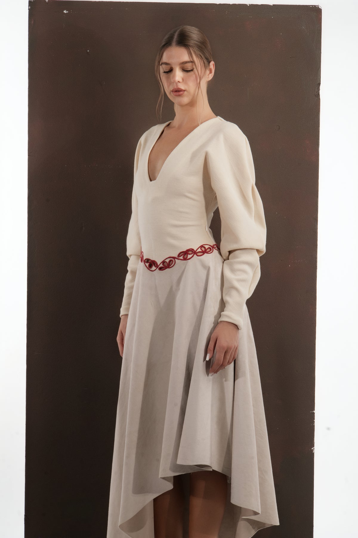 ALISADUDAJ beige wool asymmetric dress, close-up of deep V neckline, bishop sleeves and red embroidered waist motif