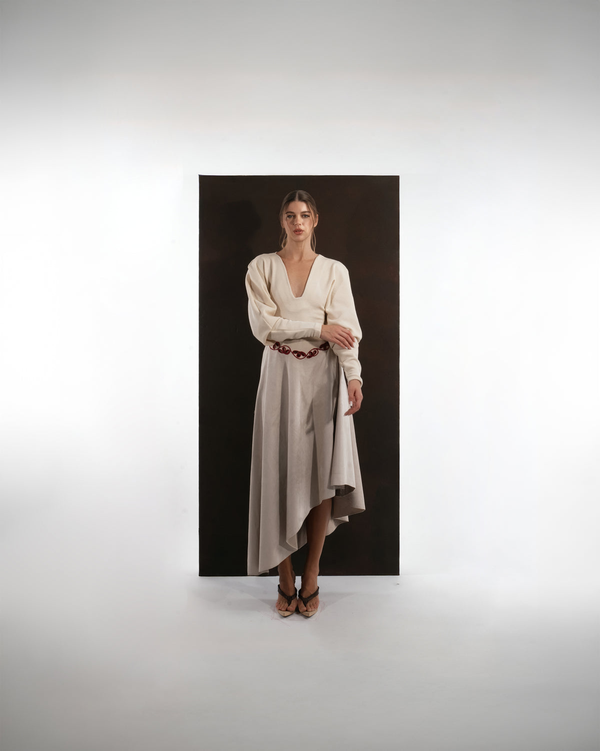 ALISADUDAJ beige wool asymmetric dress, front view with hand at waist showing bishop sleeves and asymmetric hem