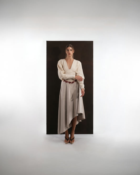 ALISADUDAJ beige wool asymmetric dress, front view with hand at waist showing bishop sleeves and asymmetric hem