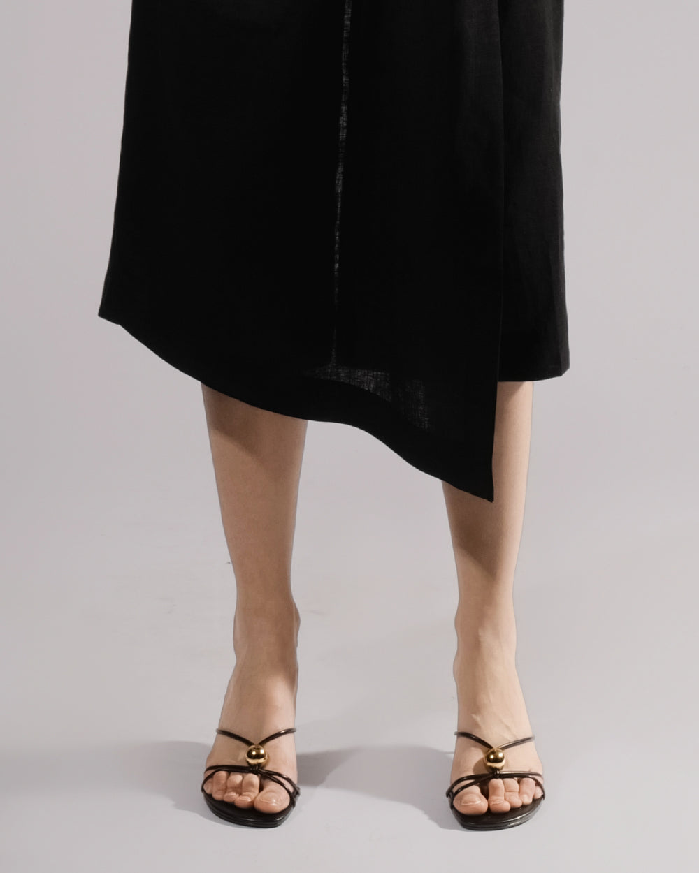 ALISADUDAJ black linen deep-V wrap top and midi skirt set, close-up of asymmetric skirt hem and strappy sandals