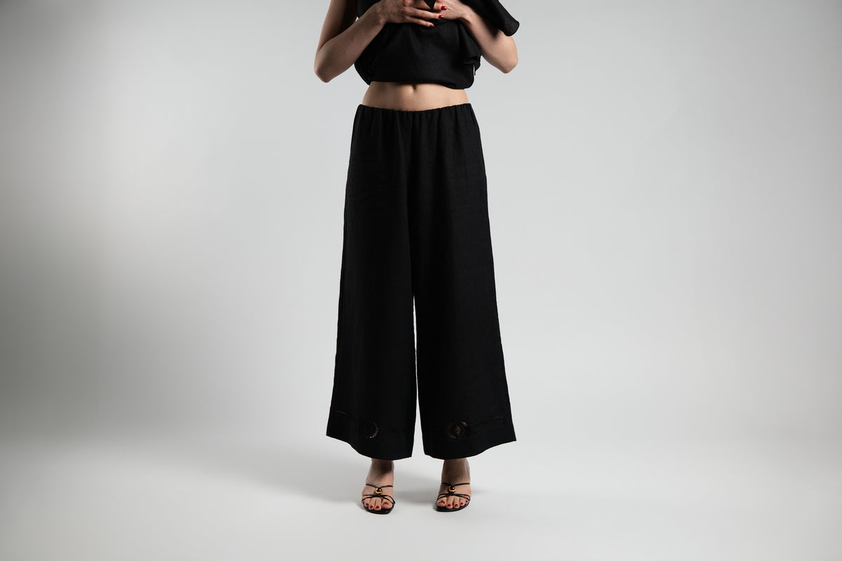 ALISADUDAJ black linen wide-leg trousers, front view showing elasticated waist and open-work hem detail