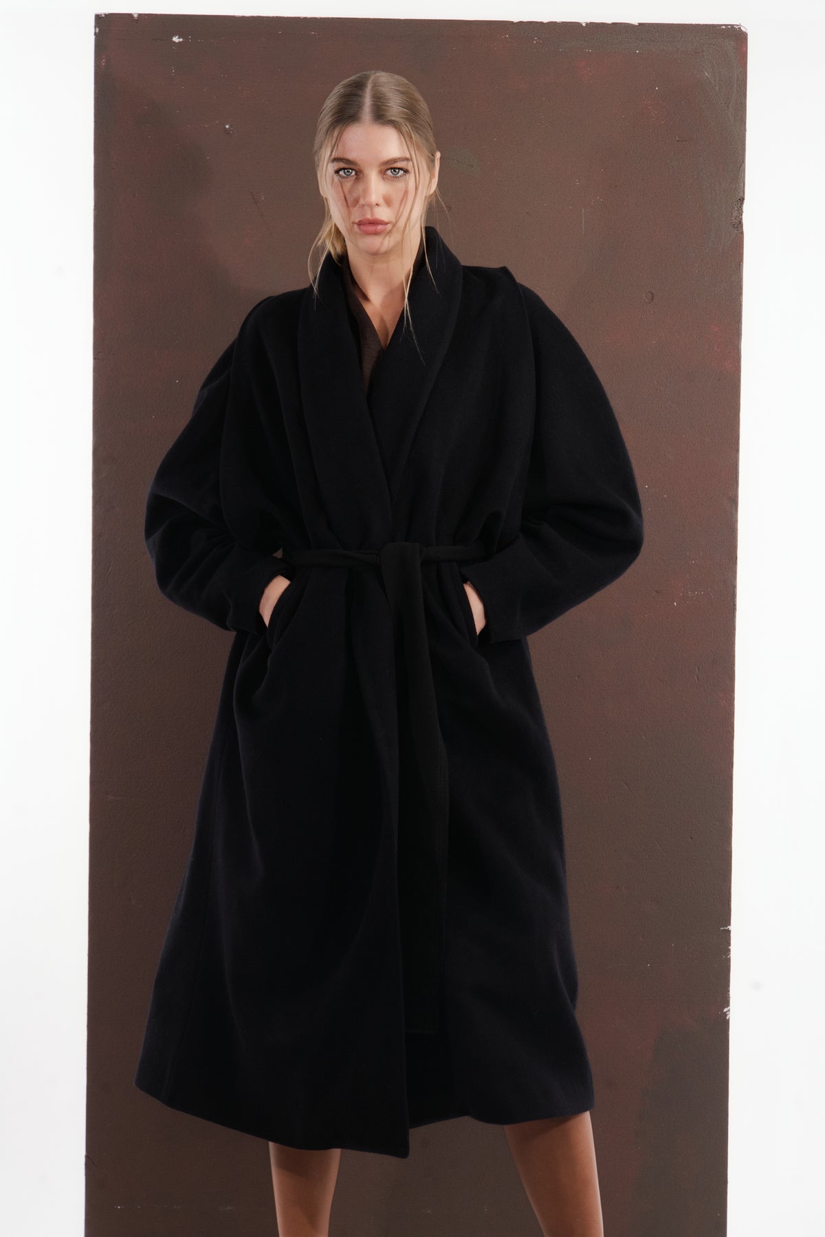 ALISADUDAJ black wool belted wrap coat, three-quarter view with hands in pockets showing coat drape