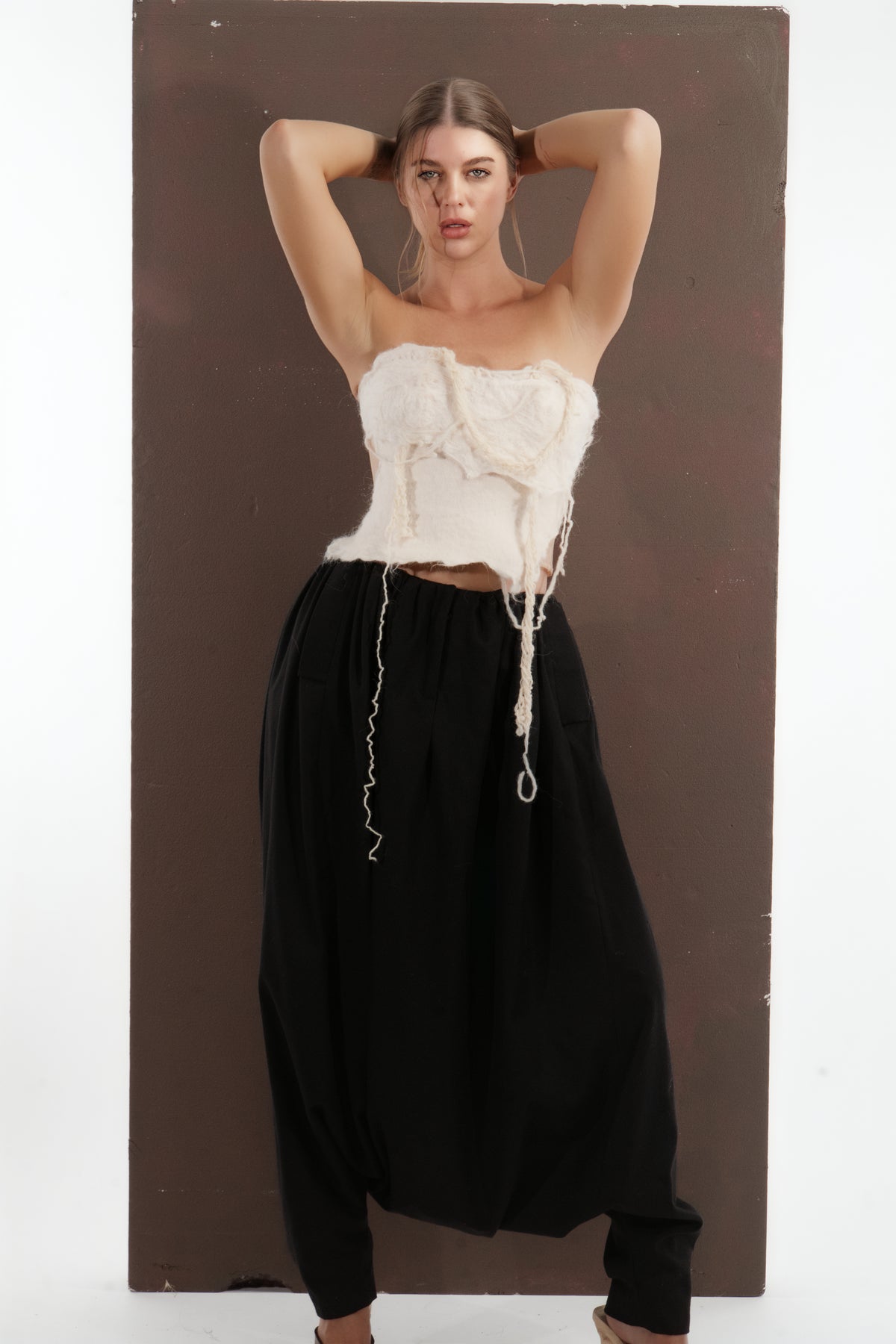 ALISADUDAJ black wool draped harem trousers, front view with arms raised showing waistband and drape
