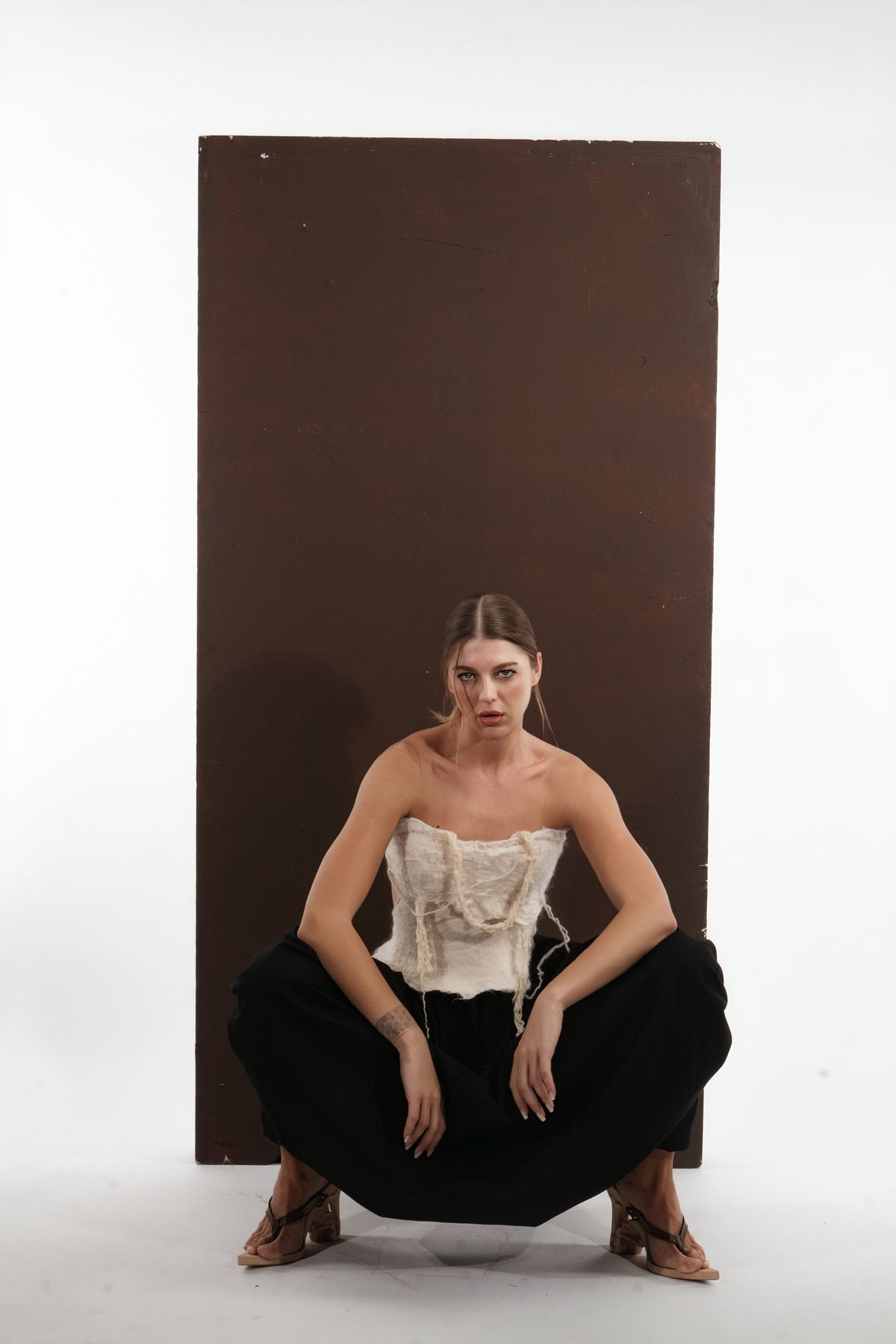 ALISADUDAJ black wool draped harem trousers, crouching front view with ivory corset top