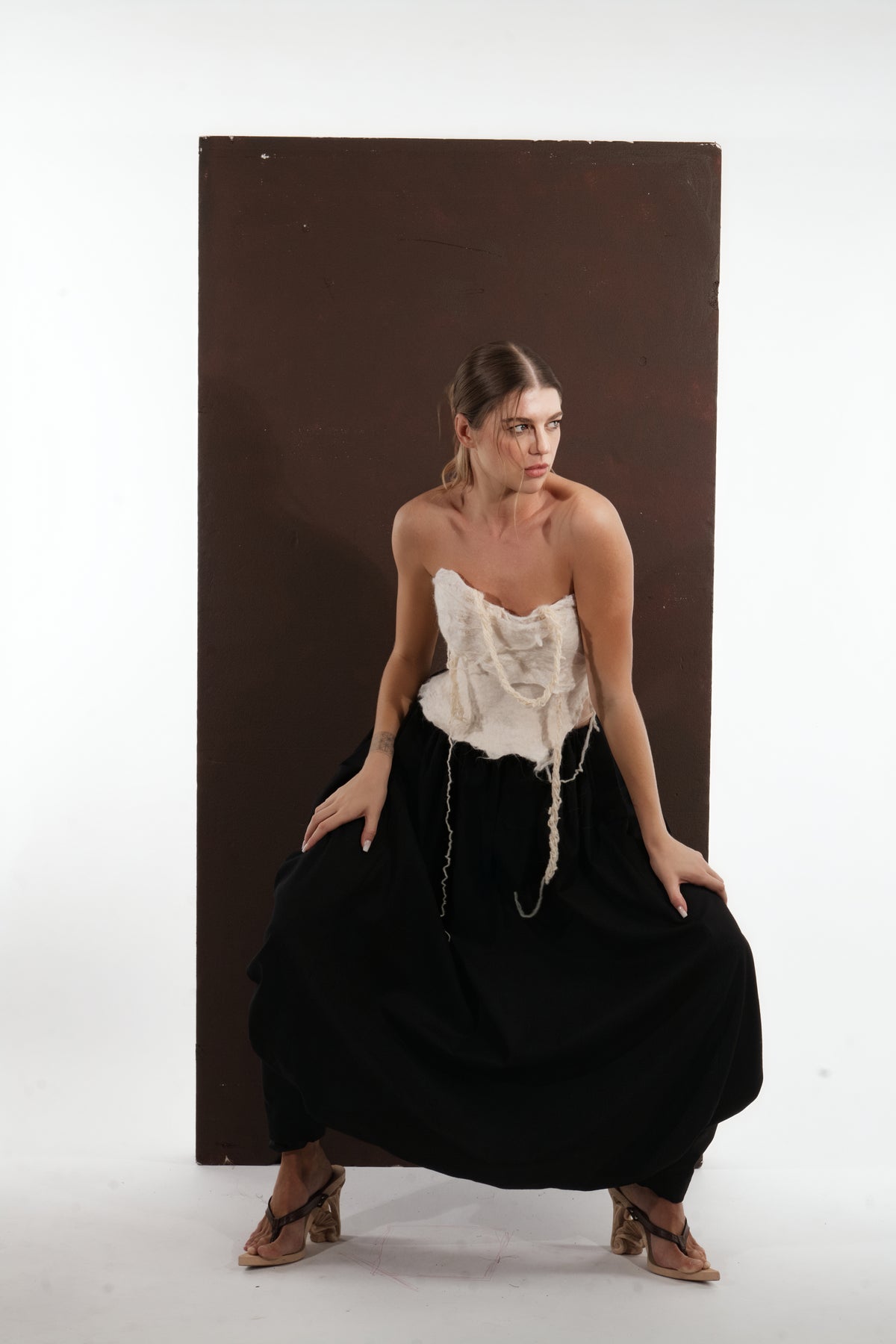 ALISADUDAJ black wool draped harem trousers, three-quarter crouching view with ivory felted corset, wool blend