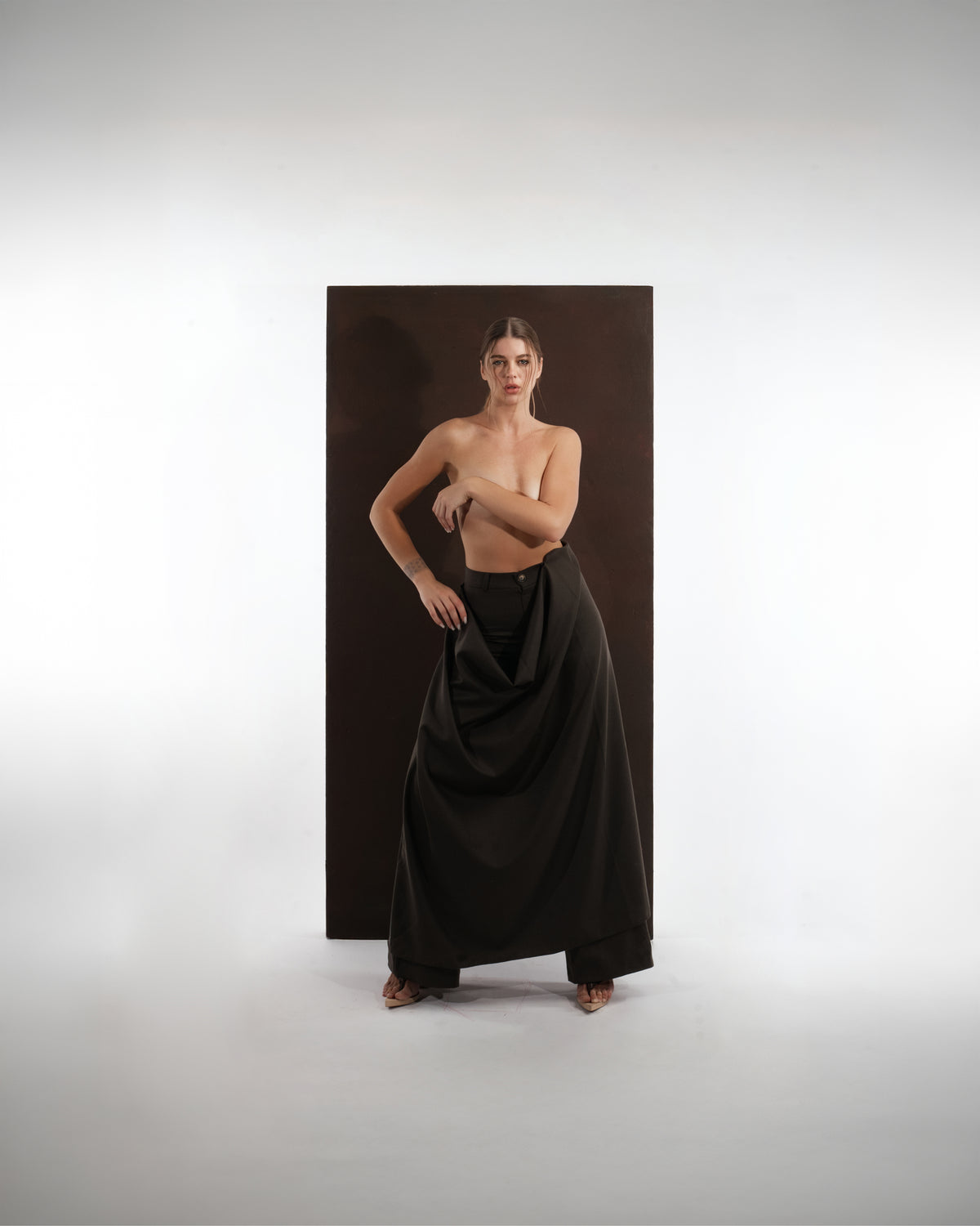 ALISADUDAJ black wool draped wide-leg trousers, three-quarter view with hand on hip showing draped panel