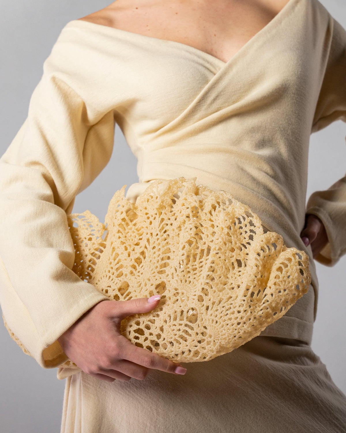 ALISADUDAJ Çantro beige resin crochet clutch bag held at the waist of the CRAFT 08 off-white wool wrap outfit, close-up