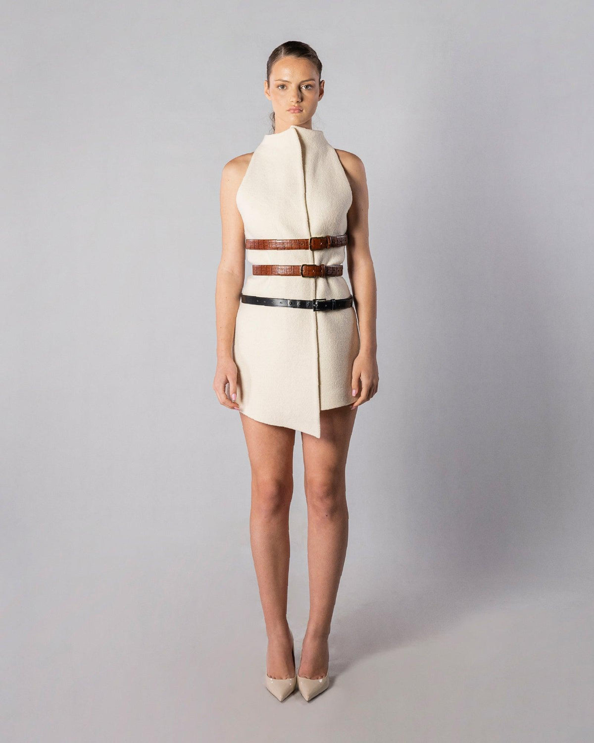 ALISADUDAJ CRAFT 03 white wool sleeveless funnel-neck mini dress with three leather belts, front view, full length, showing asymmetric wrap hem
