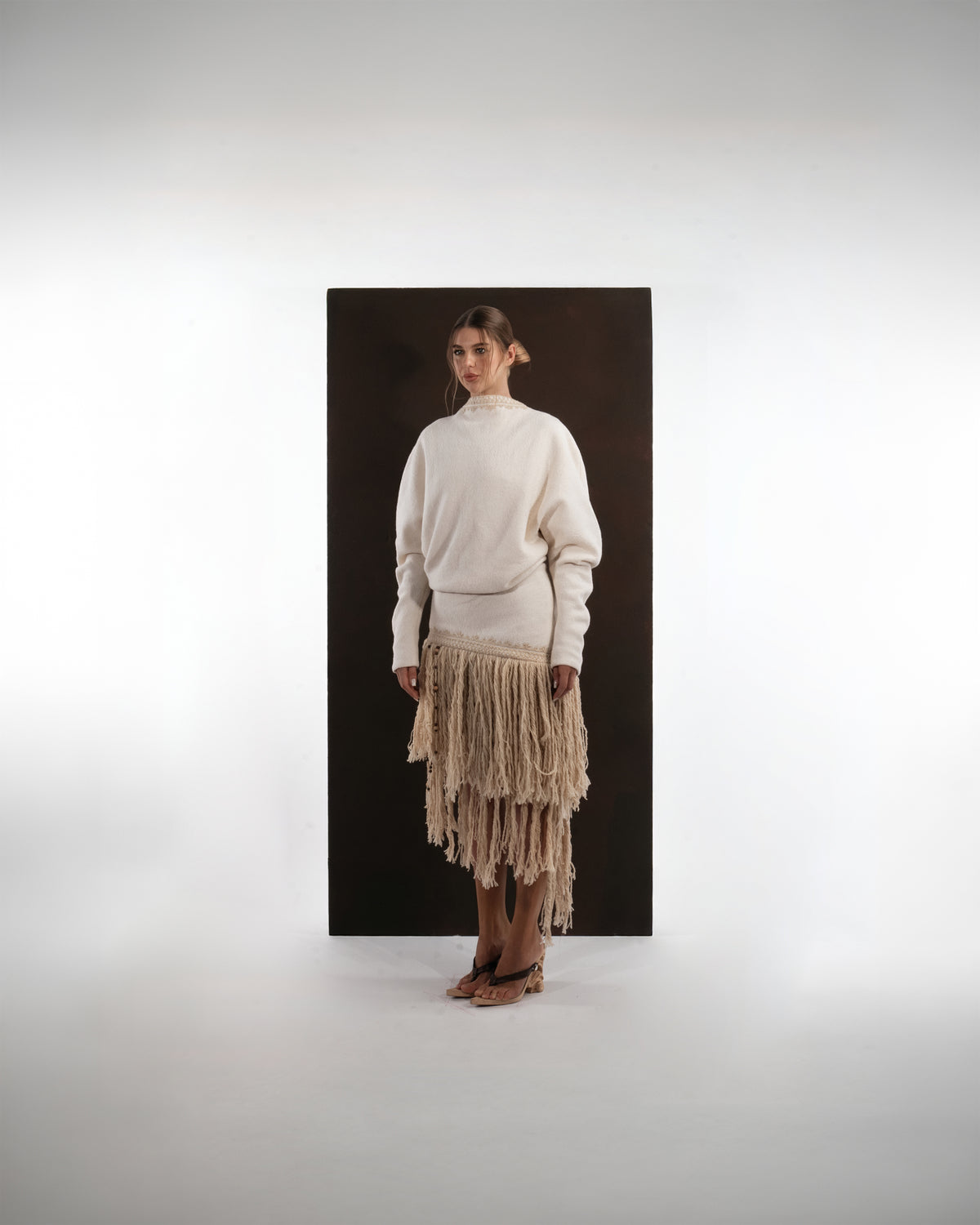 ALISADUDAJ ivory wool fringed dress, front three-quarter view showing braid-trimmed neckline and fringe skirt