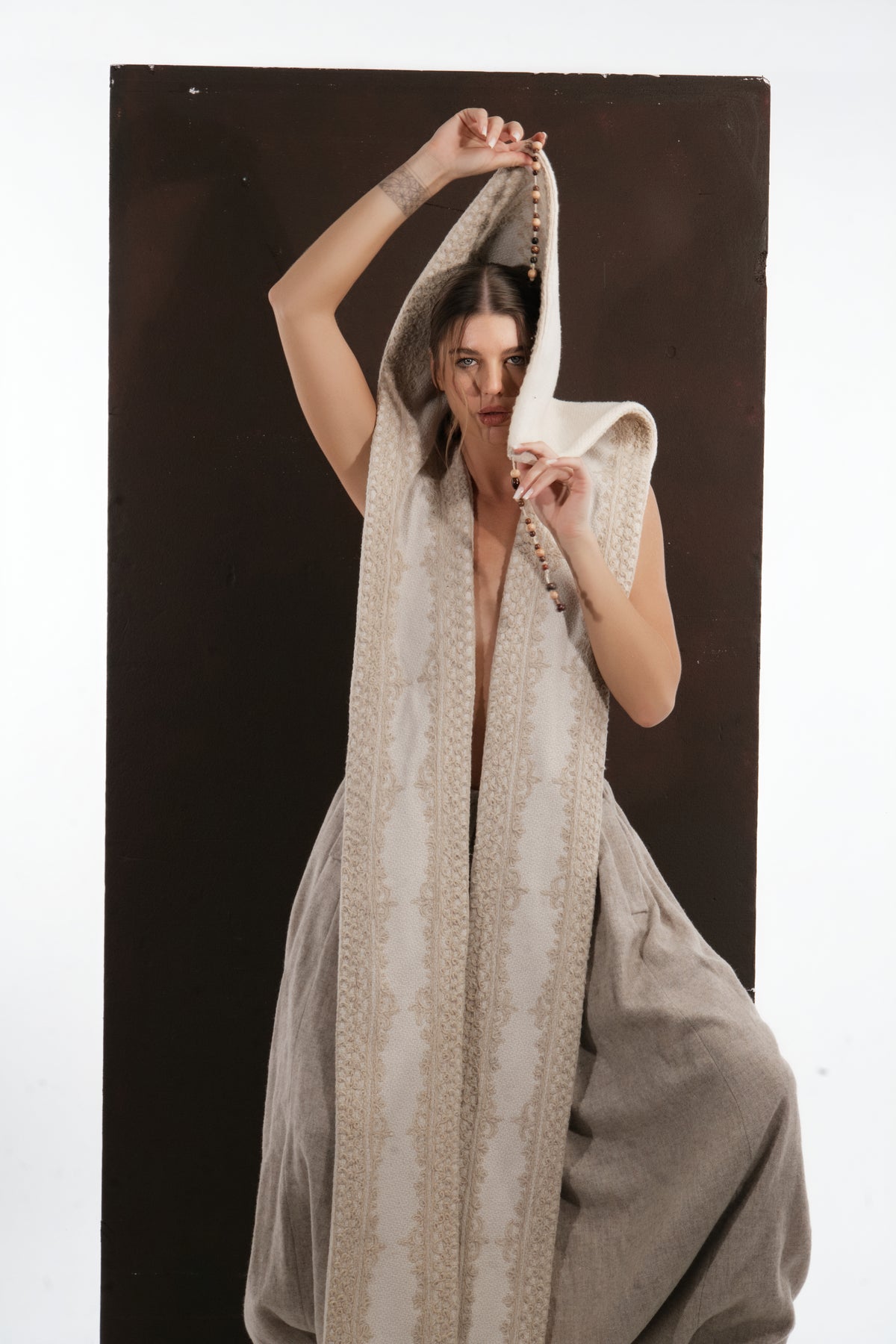 ALISADUDAJ ivory wool beaded hooded vest, close-up with hood pulled forward as a veil, beaded cord in hand