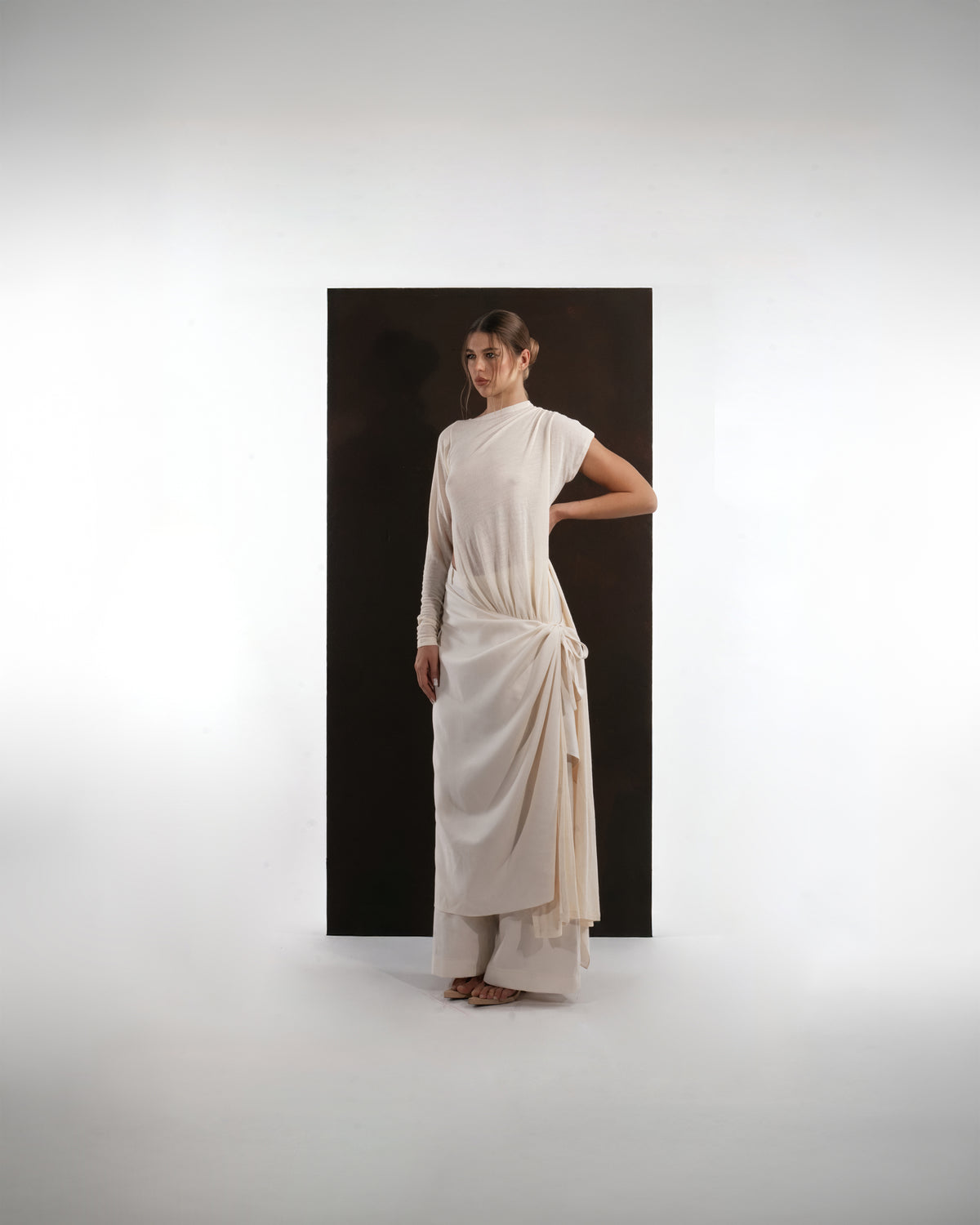 ALISADUDAJ ivory wool draped asymmetric set, three-quarter view with hand behind back showing knotted skirt drape