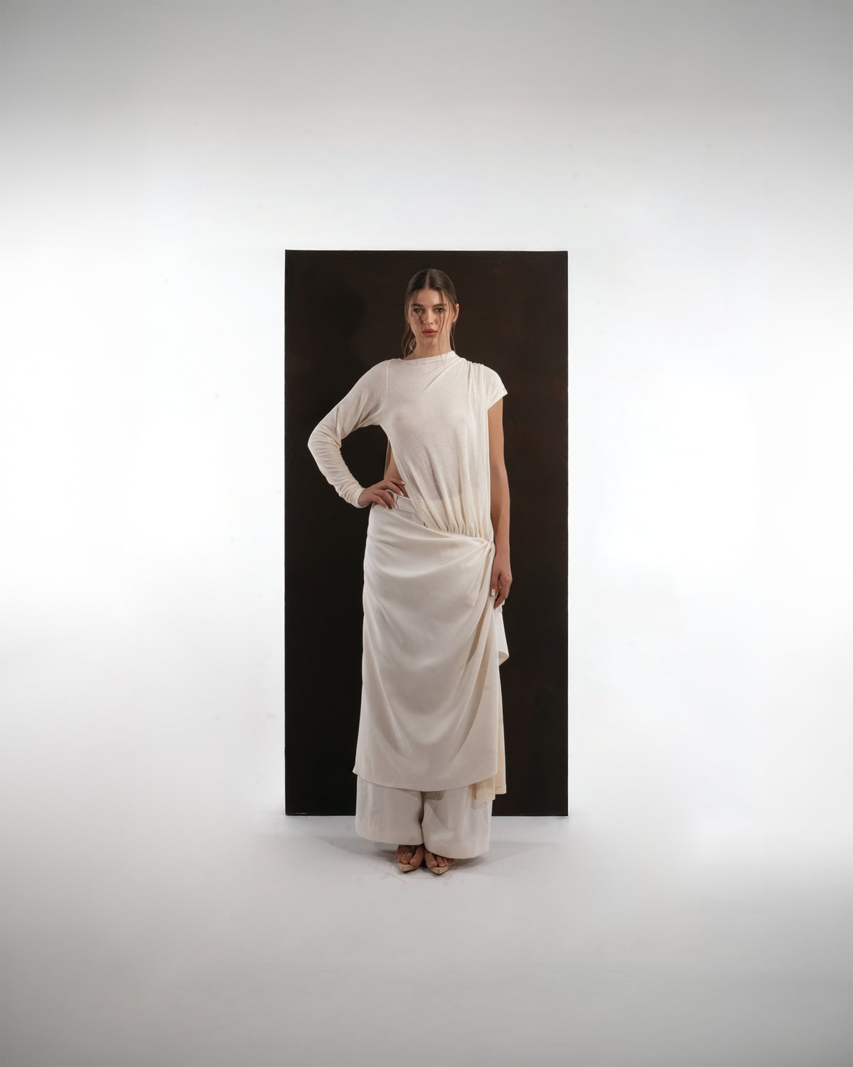 ALISADUDAJ ivory wool draped asymmetric set, front view with hand on hip showing one long sleeve and one cap sleeve