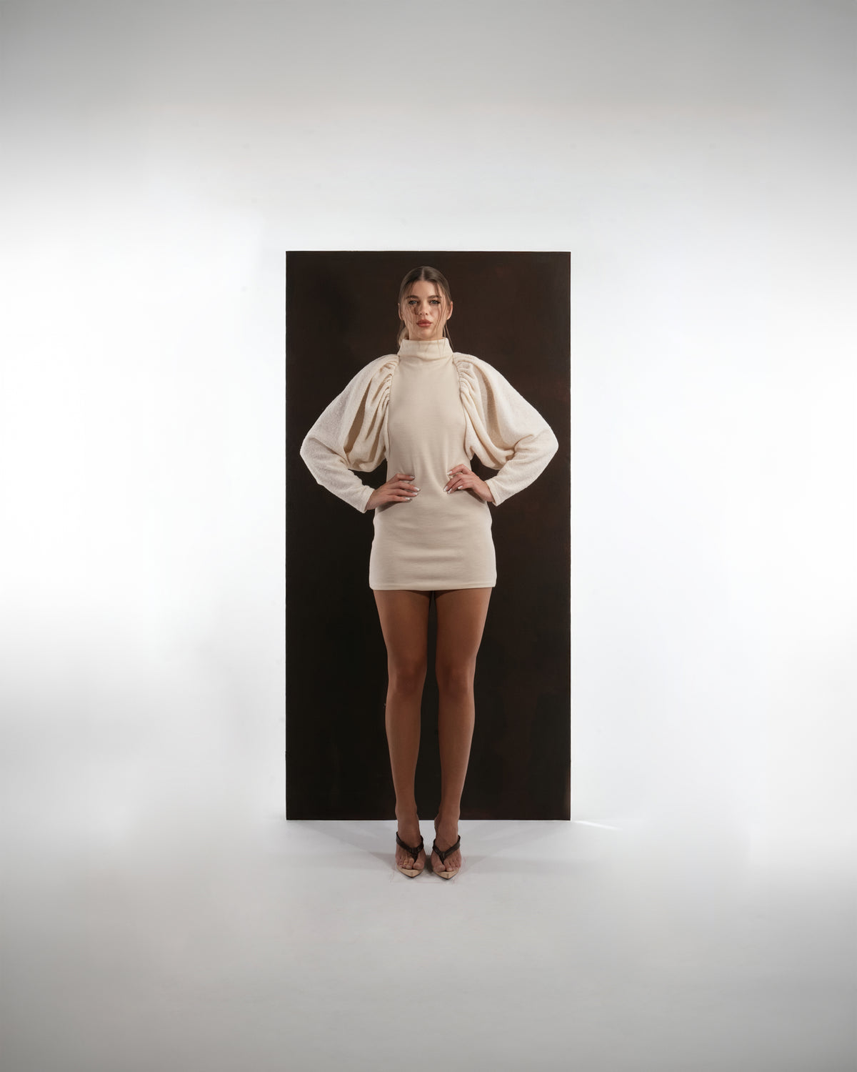 ALISADUDAJ ivory wool draped mini dress, front view with hands on hips showing sculpted sleeve volume