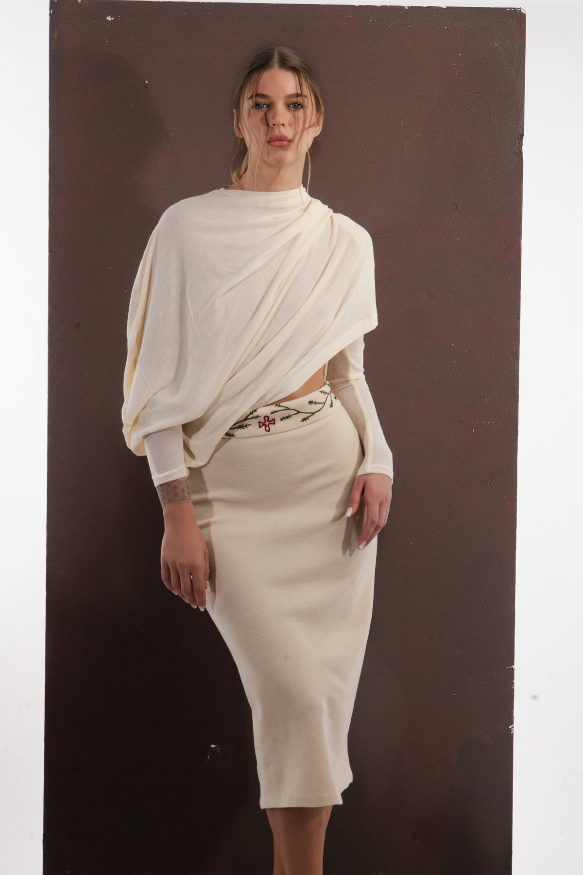 ALISADUDAJ ivory wool set, three-quarter view showing waist cut-out beneath the drape and embroidered waistband