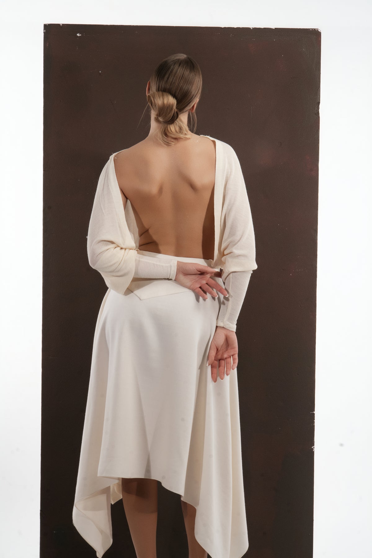 ALISADUDAJ ivory wool open-back drape dress, back view with hands behind the waist showing hem points