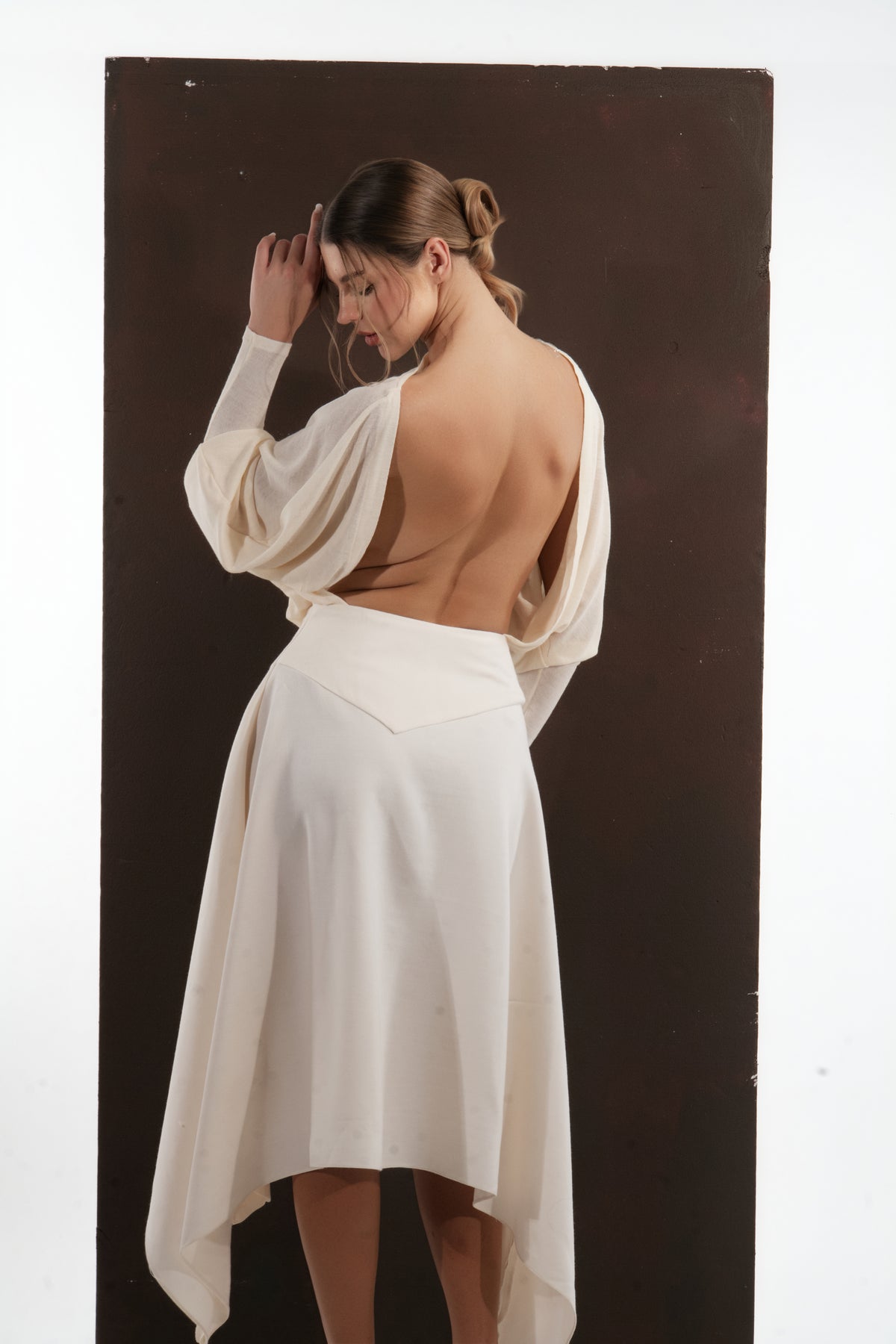 ALISADUDAJ ivory wool open-back drape dress, back view with arm raised showing open back and waist yoke