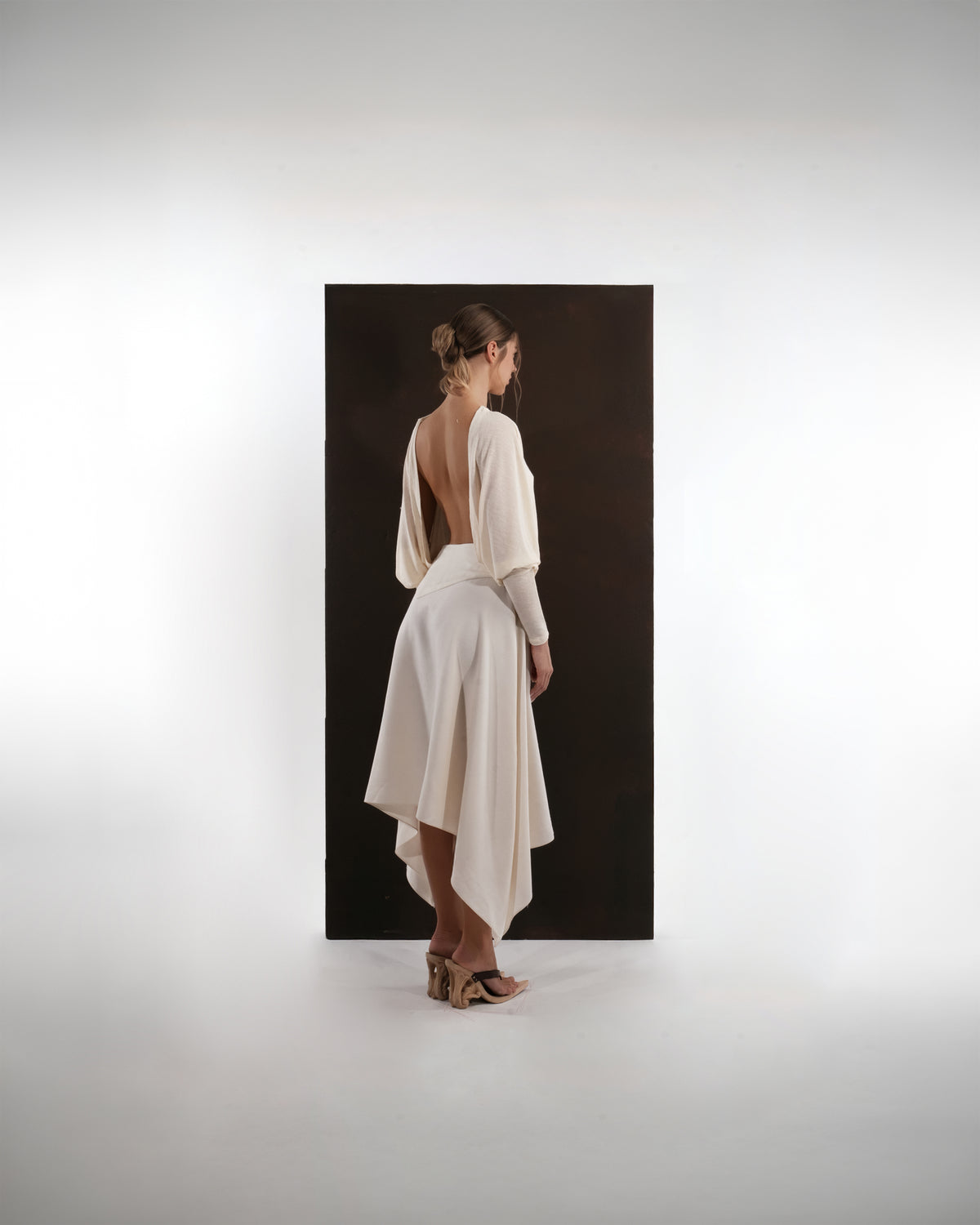 ALISADUDAJ ivory wool open-back drape dress, side back view showing draped sleeve and asymmetric hem