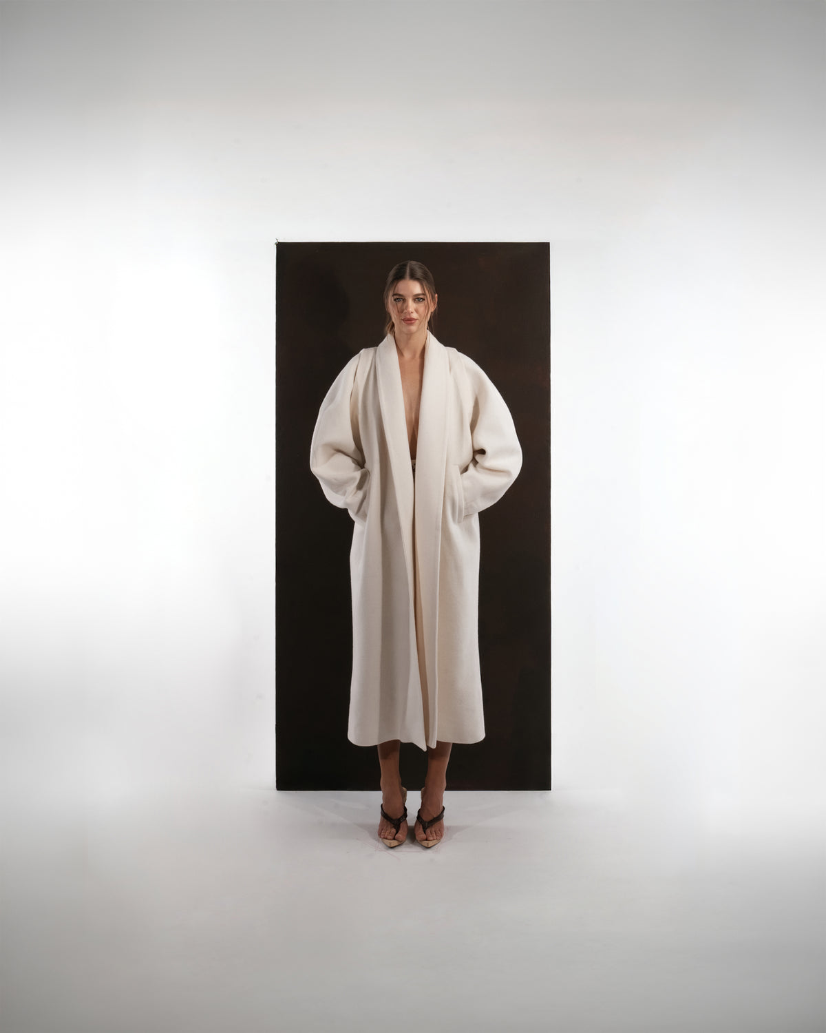 ALISADUDAJ ivory wool cocoon coat, front view with hands in pockets showing draped shawl collar